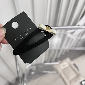 Détail d'une pince à cheveux avec nœud crème sur carte noire, tenue à la main par l'usager