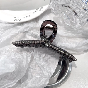Detail showing elegant grey acrylic hair claw with rhinestones and pearls on white setup