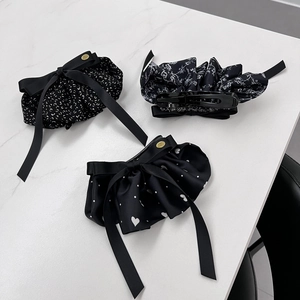 Tre eleganti pinze per capelli in raso nero con motivi floreali su base di marmo