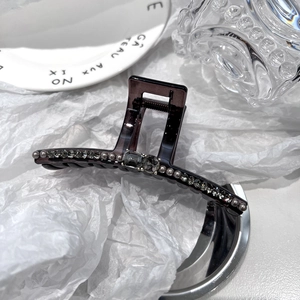 Detailed close-up of dark purple hair claw with crystals and pearls on white backdrop