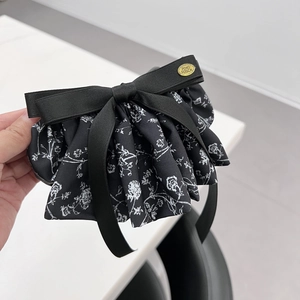 Dettaglio della molletta per capelli a fiocco nero floreale con logo in metallo dorato