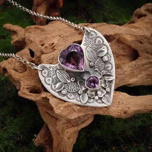 Vintage silver alloy heart necklace with large purple gemstone on natural mossy wood base