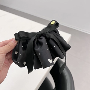 Dettaglio della pinza per capelli a fiocco in raso nero con pois e placca dorata