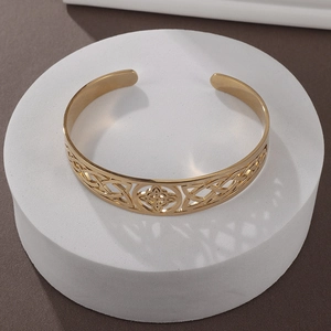 Detail of gold hollow open bangle featuring clover motif and Celtic knot patterns