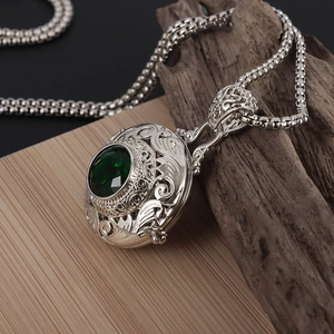 Vintage silver hollow pendant necklace with large faceted green gemstone on wood