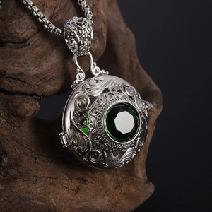 Macro shot of silver hollow spherical pendant with emerald green stone on wood