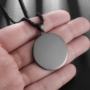 Macro view of a matte black round stainless steel pendant on a box chain held in hand