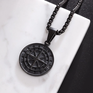 Macro shot of matte black compass pendant on box chain over a marble background