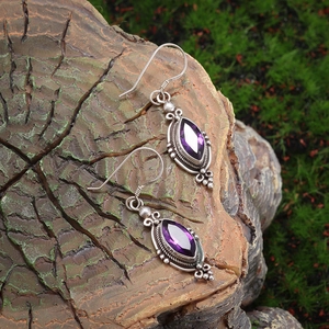 Macro shot of purple marquise-cut amethyst earrings on rustic wood and moss background