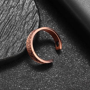 Macro shot of Celtic knot relief on a copper magnetic therapy ring over a dark textured stone