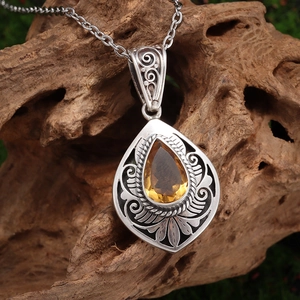 Macro shot of vintage silver teardrop pendant with a yellow gemstone on a rustic branch
