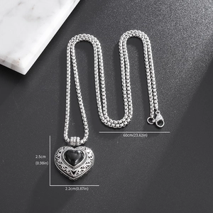 Collier médaillon cœur vintage avec pierre noire et motif creux argenté sur marbre