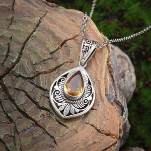 Detail of tear-drop yellow gemstone with antique silver floral engraving on tree bark