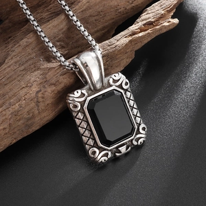 Close-up of vintage silver square pendant with black gemstone on a rustic wooden log