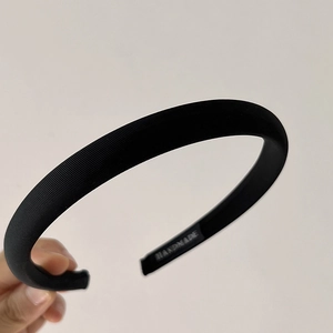 Detail of a black twill fabric headband with handmade label and sponge padding