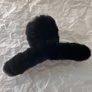 Détail d'une grande pince à cheveux en peluche noire sur fond de papier blanc texturé