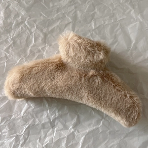 Close-up of a large fluffy faux fur hair claw clip in beige on white background