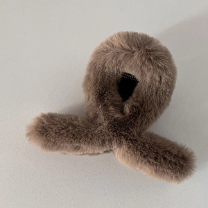 Détail de la texture en fausse fourrure douce et du design croisé sur la pince à cheveux taupe