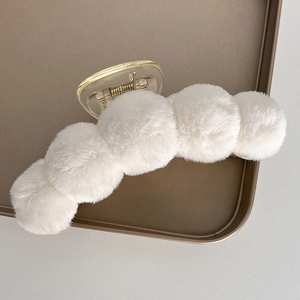 Detail of soft white faux fur claw clip with plush pom-poms on a display tray