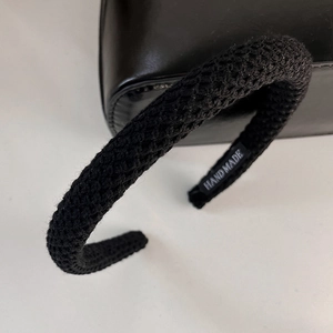 Detail of black knitted headband featuring a handmade label and textured yarn weave