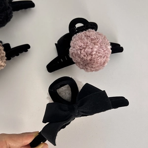 Close-up of black velvet bow and plush pom-pom hair claws for winter styling