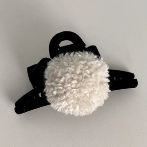 Detail of a black hair claw clip featuring a large white faux fur ball and ribbon bow