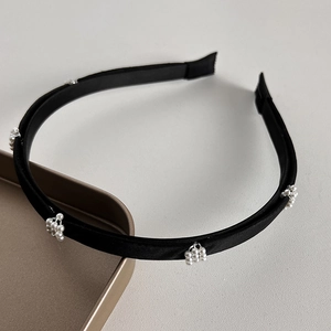 Détail d'un serre-tête en satin noir orné de grappes de perles élégantes sur un plateau