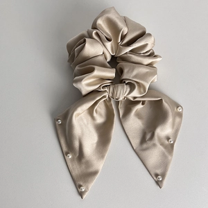 Close-up of champagne satin scrunchie with long ribbons and elegant pearl accents