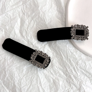 Detail of two black velvet hair clips featuring sparkling square rhinestone buckles