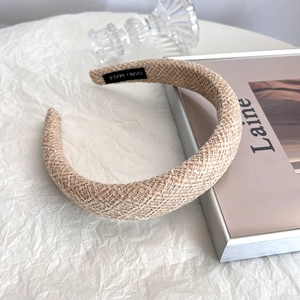 Close-up of beige wide braided headband with HAND MADE label on textured background