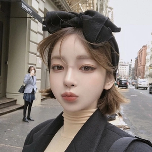 Fashionable black knit headband with large bow detail shown on a model in urban street setting