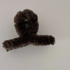 Détail d'une pince à cheveux en peluche marron foncé avec fausse fourrure et ressort doré