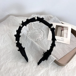 Détail d'un serre-tête en tricot noir avec bords effilochés et perles blanches chic
