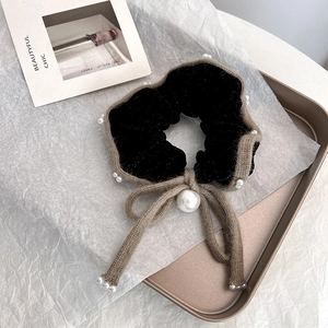 Dettaglio scrunchie in velluto con fiocco in maglia e perle su vassoio d'oro