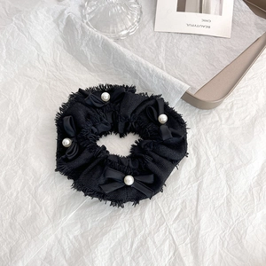 Détail d'un chouchou en tweed noir avec nœuds en satin et perles sur fond minimaliste