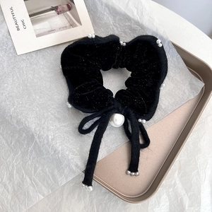 Dettaglio macro dello scrunchie in velluto nero con perle e fiocco elegante