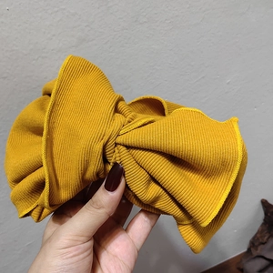 Detail of ginger yellow rib-knit headband featuring a large bow and ribbed texture