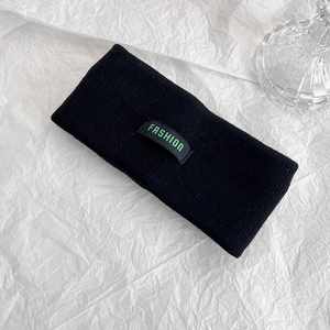 Dettaglio della fascia in maglia nera con etichetta Fashion verde su sfondo bianco