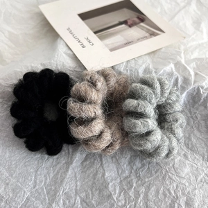 Three wool spiral hair ties in black, brown, and grey on a minimalist white backdrop