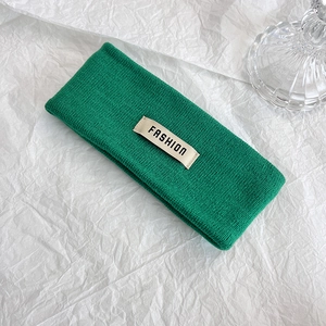 Dettaglio della fascia in maglia verde con etichetta 'FASHION' crema su sfondo bianco