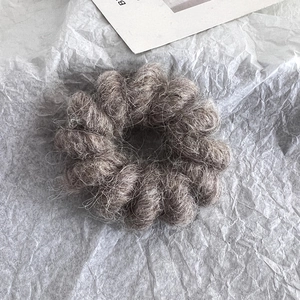Close-up of a dark grey wool spiral hair tie with soft fuzzy texture on white paper