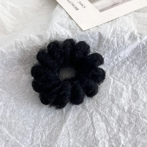Detail of a soft black wool hair tie with a textured wavy design on a white paper background