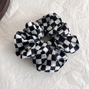 Dettaglio di scrunchie in velluto a scacchi con pieghe morbide e motivo elegante bianco e nero