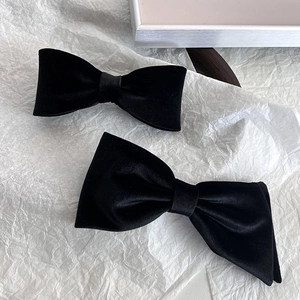 Pair of elegant black velvet bow hair clips displayed on minimalist white decor