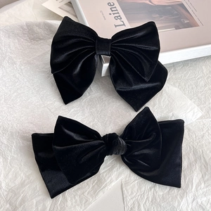 Detailed view of two elegant black silk velvet bow hair clips on a chic fashion magazine