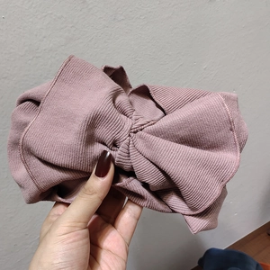 Detail of knitted bow headband showing rose pink ribbed texture and fine edge stitching