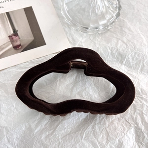 Close-up of a large brown flocked hair claw clip on a minimalist textured background