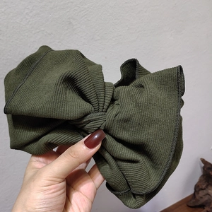 Close-up of olive green knitted headband featuring a large bow and ribbed texture