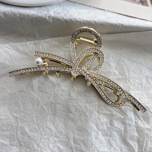 Detailaufnahme einer goldenen Schleifen-Haarklammer mit Strasssteinen und weißer Perle