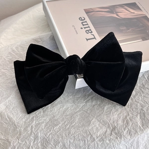 Close-up of elegant black velvet bow hair clip on a minimalist aesthetic background